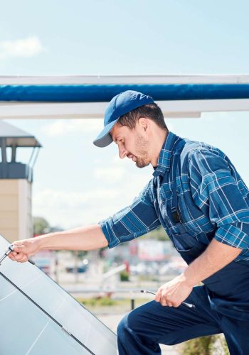 Young technician master in workwear bending over solar panel on the roof